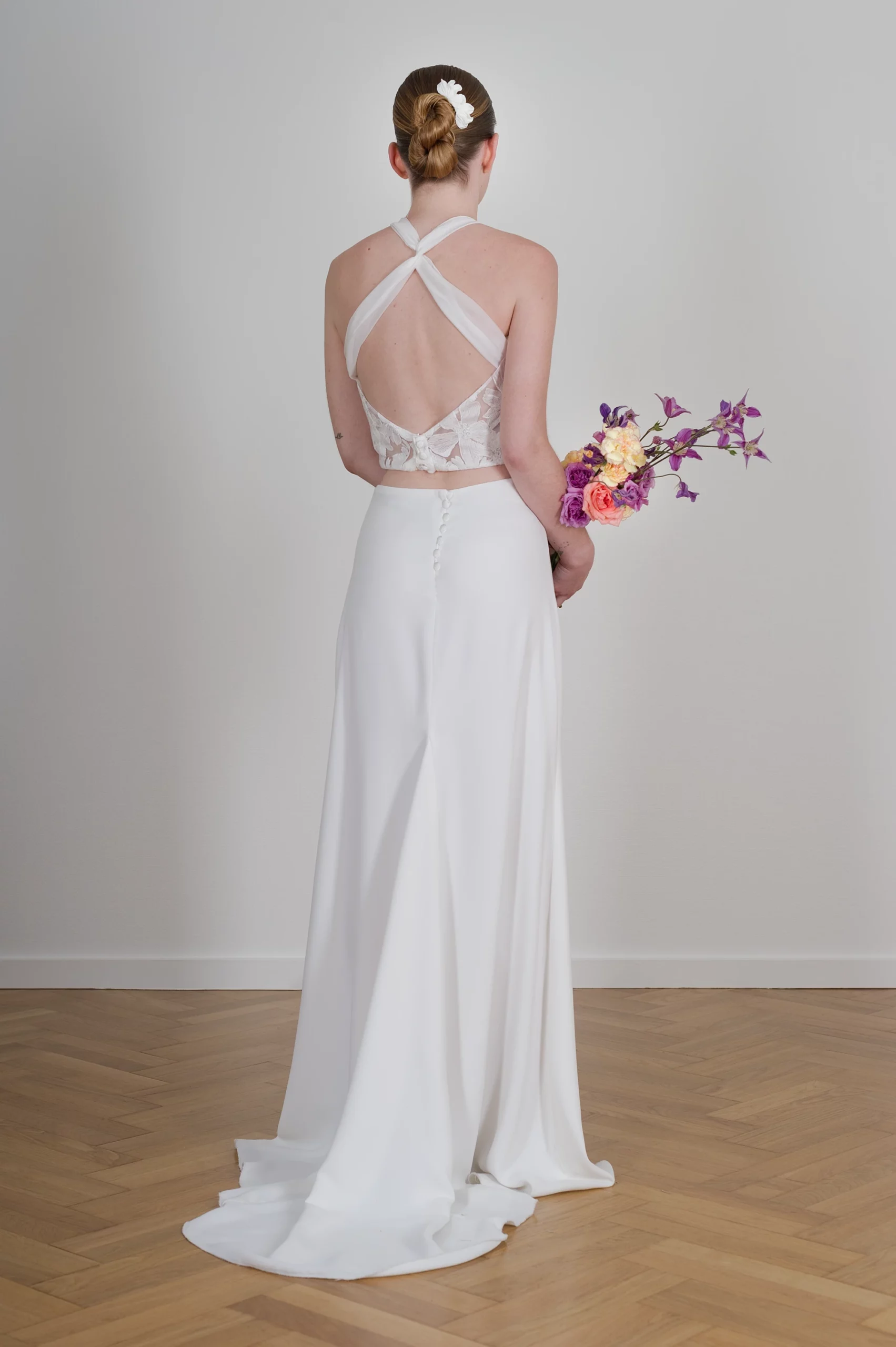 Mariée de dos avec robe dos nu croisé et bouquet de fleurs colorées.