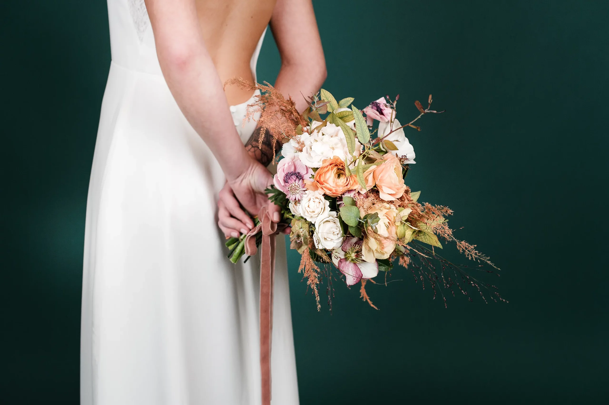 Vue arrière de la robe de mariée 'Garance' avec un bouquet de fleurs fraîches dans les mains de la mariée, mettant en valeur le dos ouvert de la robe.