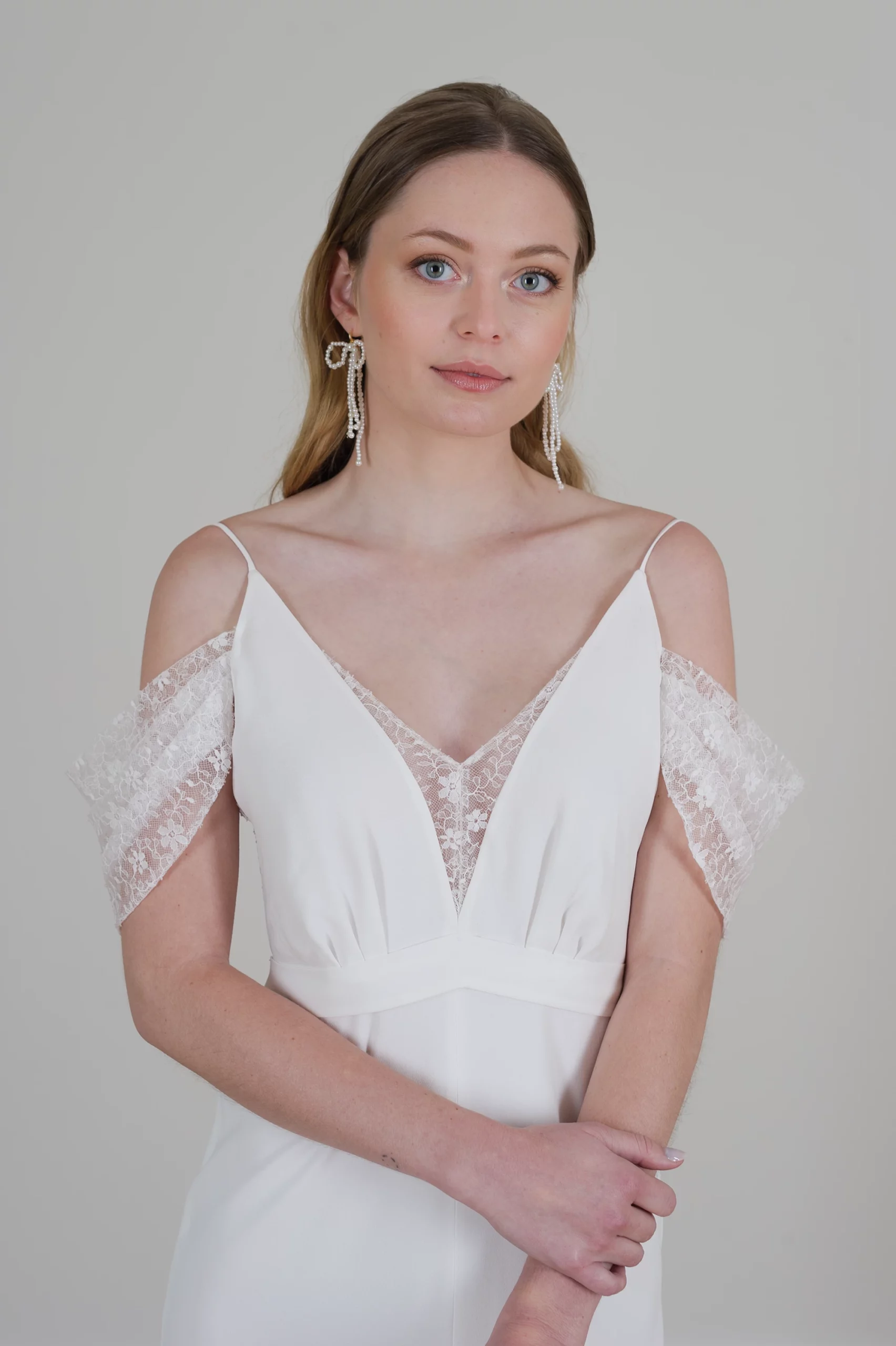 Mariée en robe avec décolleté en V, manches en dentelle et boucles d'oreilles pendantes.