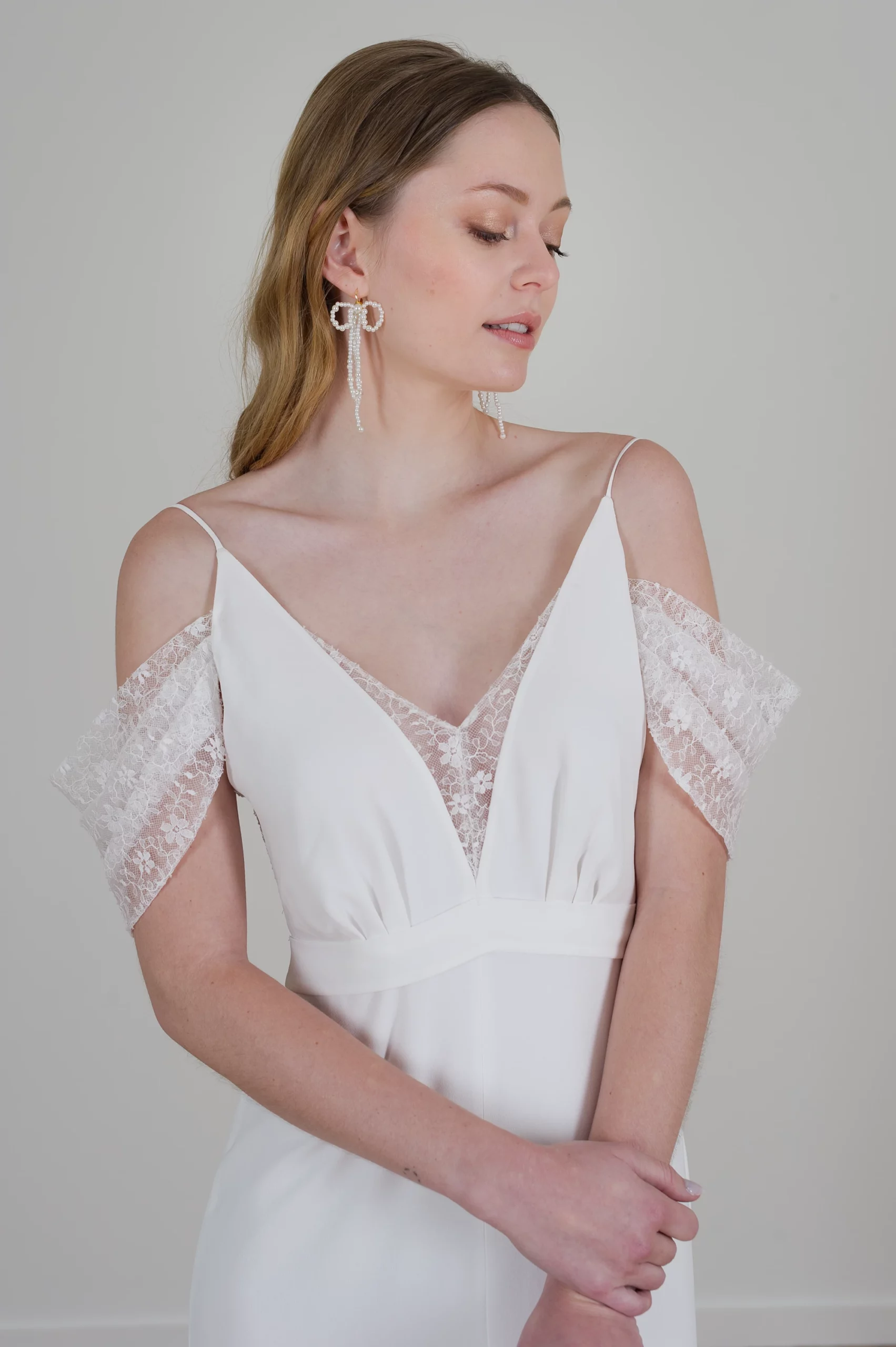 robe-de-mariee-toulouse-manon-06 Mariée en robe avec décolleté en V, manches en dentelle et boucles d'oreilles pendantes.