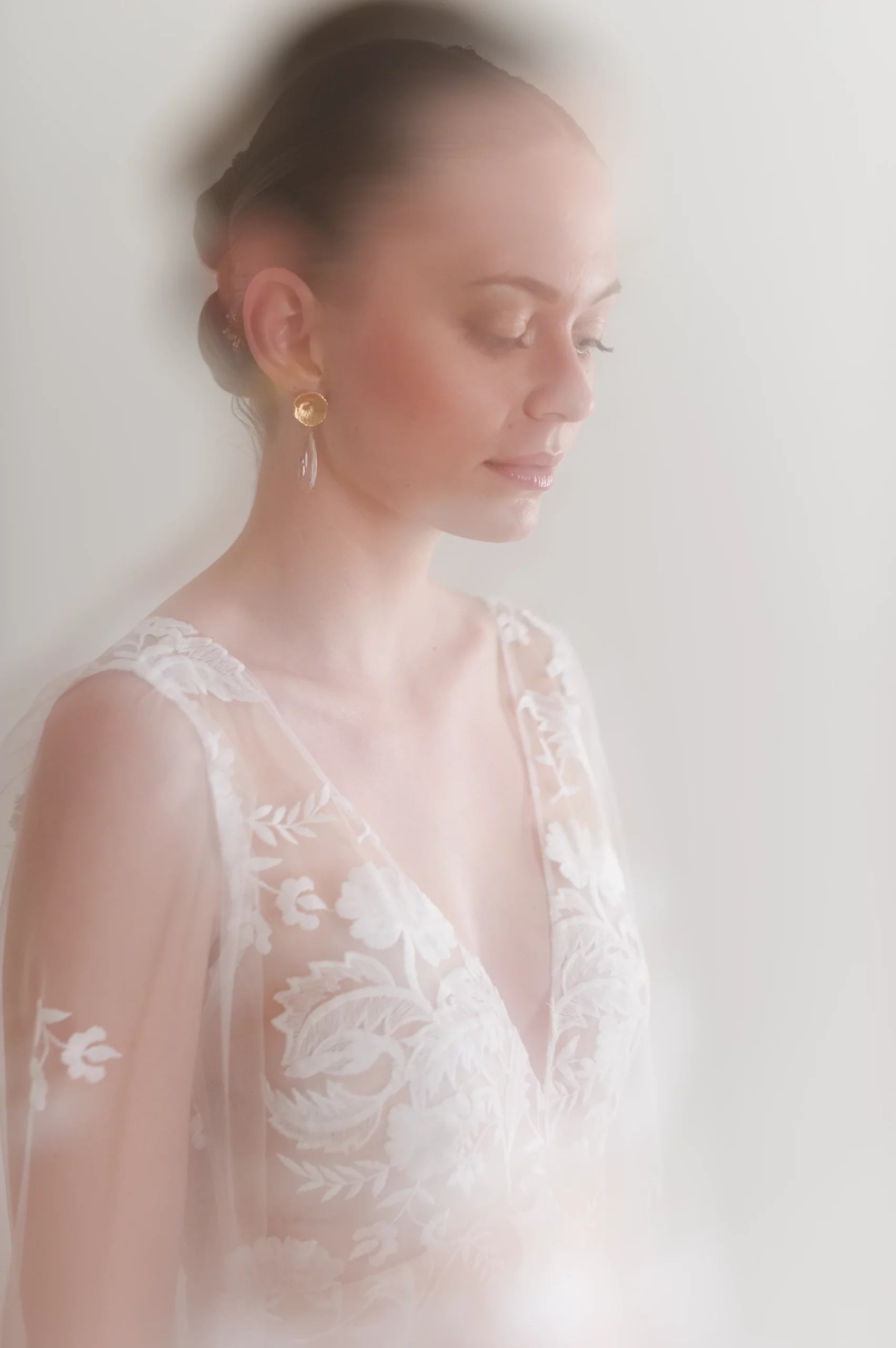 Portrait flou de la mariée portant la robe de mariée Sophia avec broderies florales et boucles d'oreilles dorées