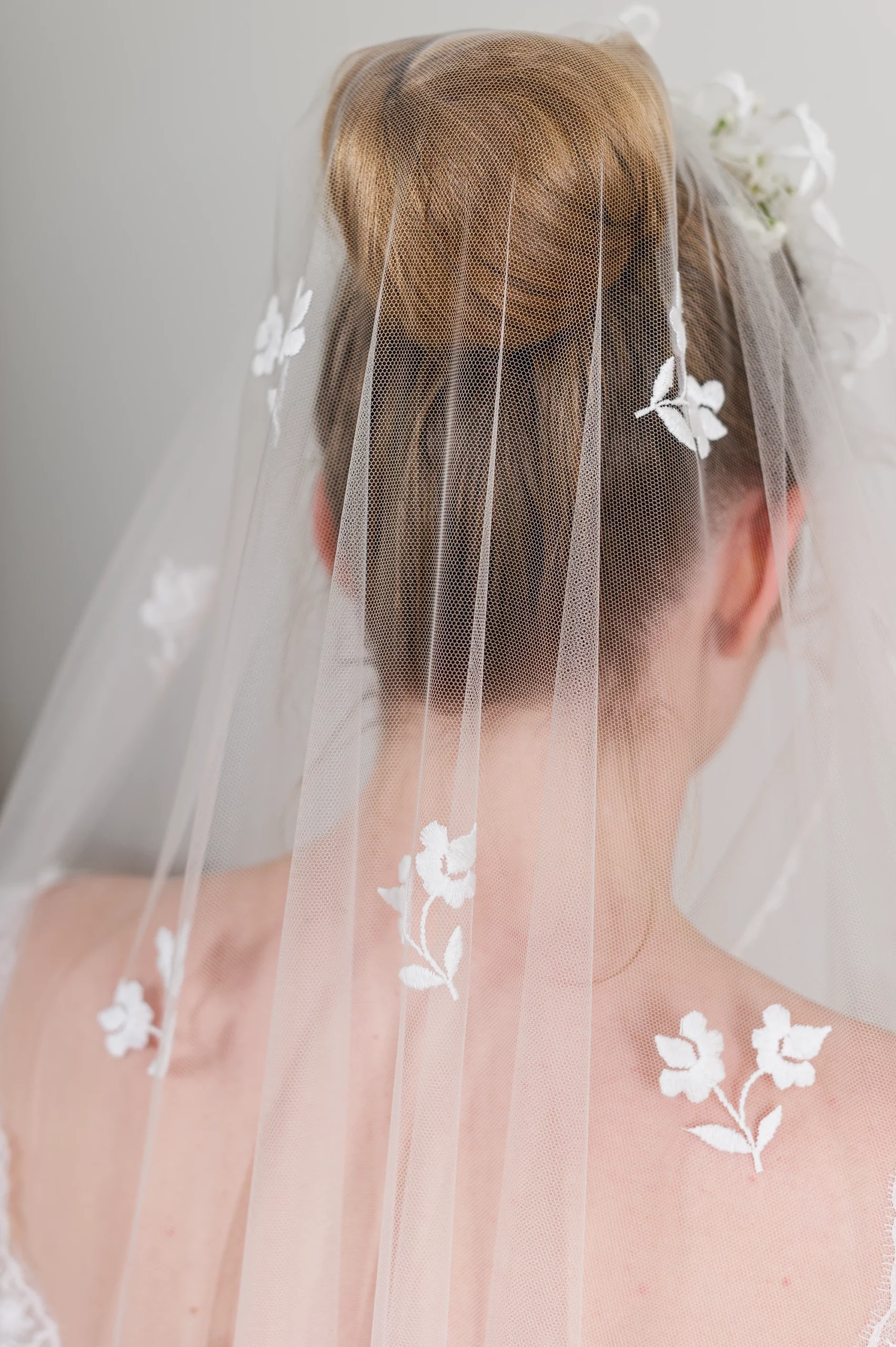 Vue de dos d'un chignon bas de mariée orné d'un voile en tulle brodé de motifs floraux, tombant délicatement sur ses épaules.