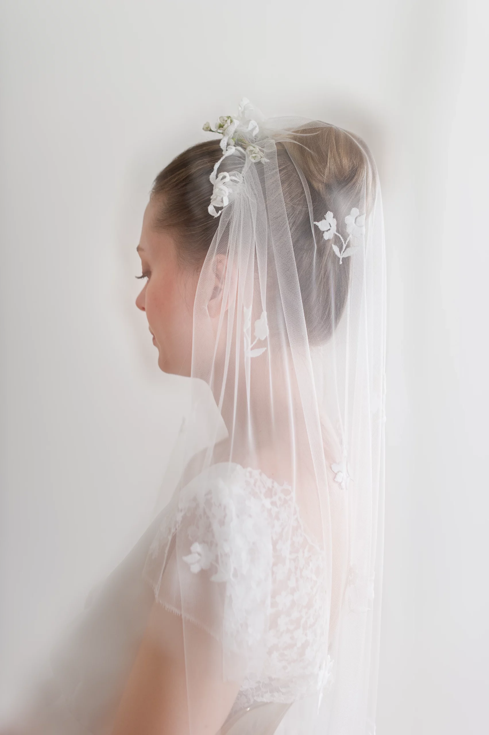 Profil de mariée avec un voile en tulle finement brodé de fleurs, porté avec un chignon élégant et orné de délicates fleurs naturelles.