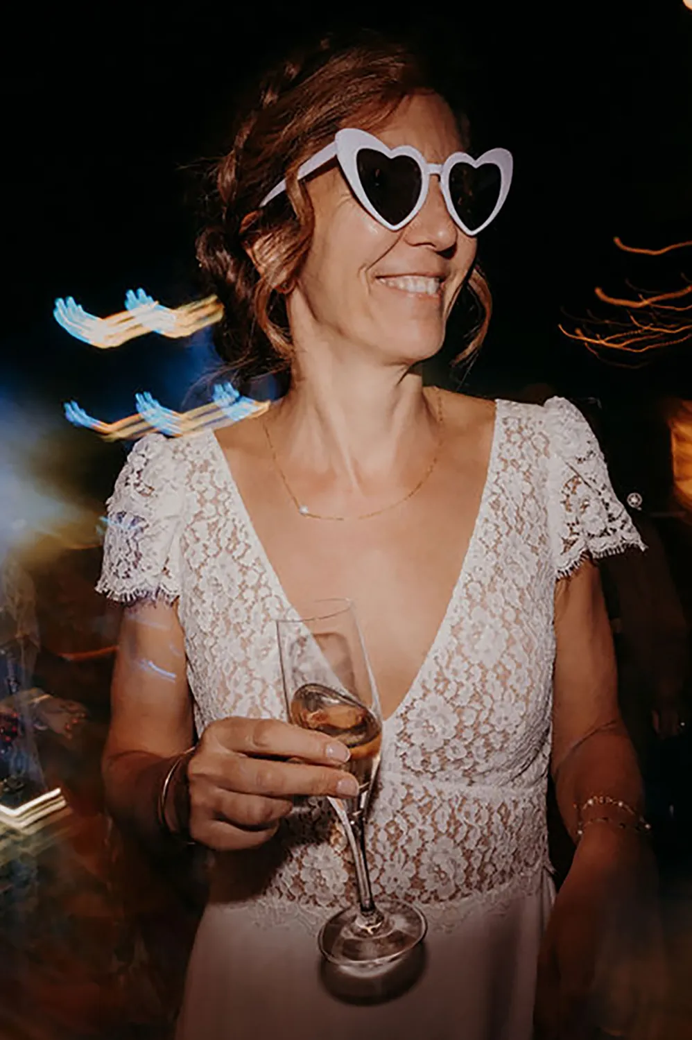 Gwenaël - Robe de mariée en Dentelle de Calais – Création sur mesure Louise Dentelle à Toulouse Mariée souriante en robe Louise Dentelle en Dentelle de Calais, tenant une coupe de champagne pendant la fête de mariage.