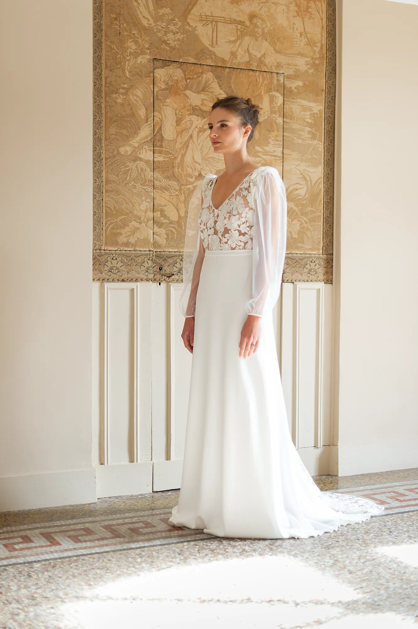 Robe de mariée Alma vue en pied, top brodé floral transparent et manches en tulle, silhouette fluide en crêpe. Création Louise Dentelle.