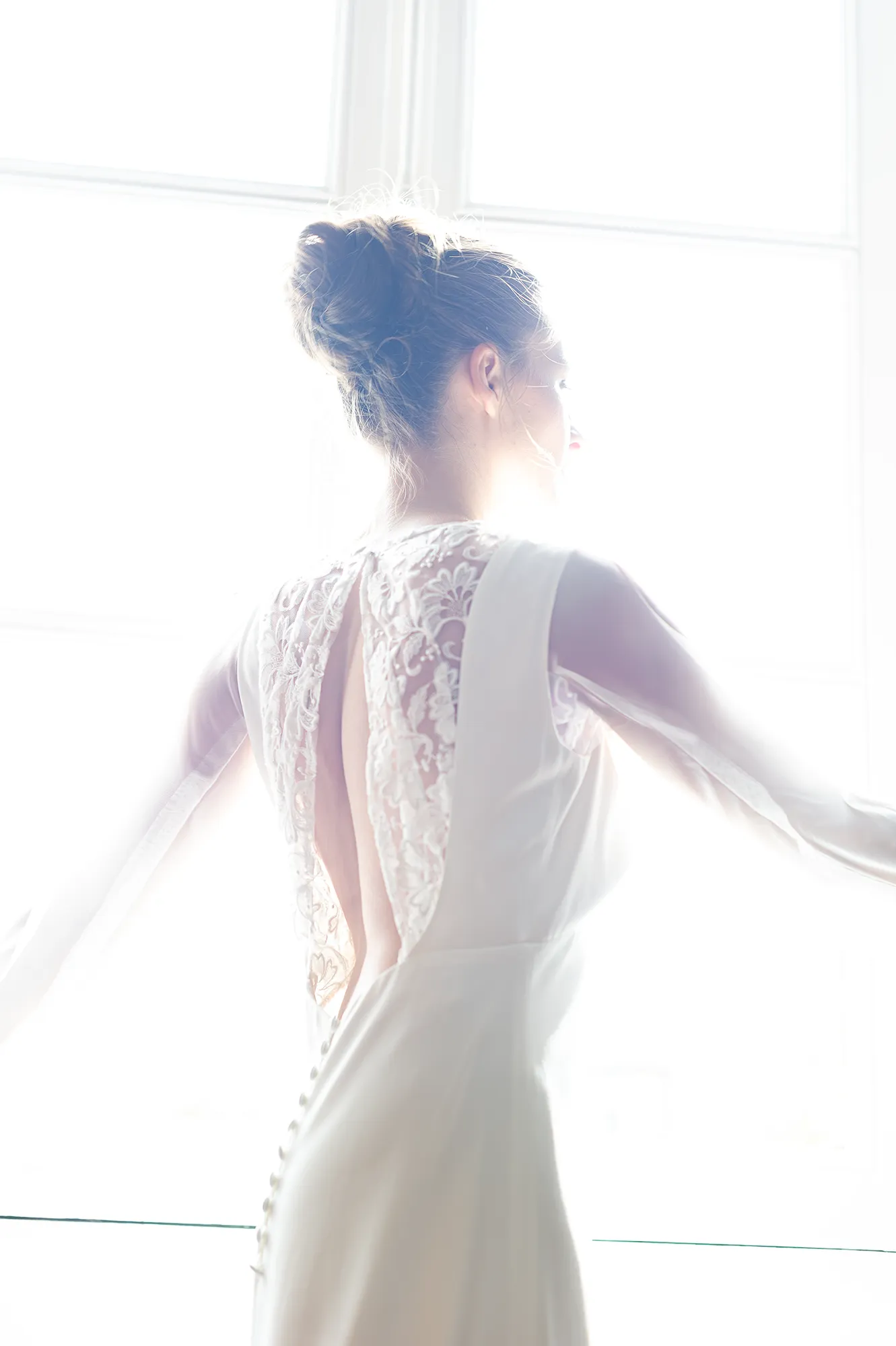 Robe de mariée Elena vue de dos en contre-jour, dentelle brodée, manches en tulle et boutons recouverts. Création Louise Dentelle.