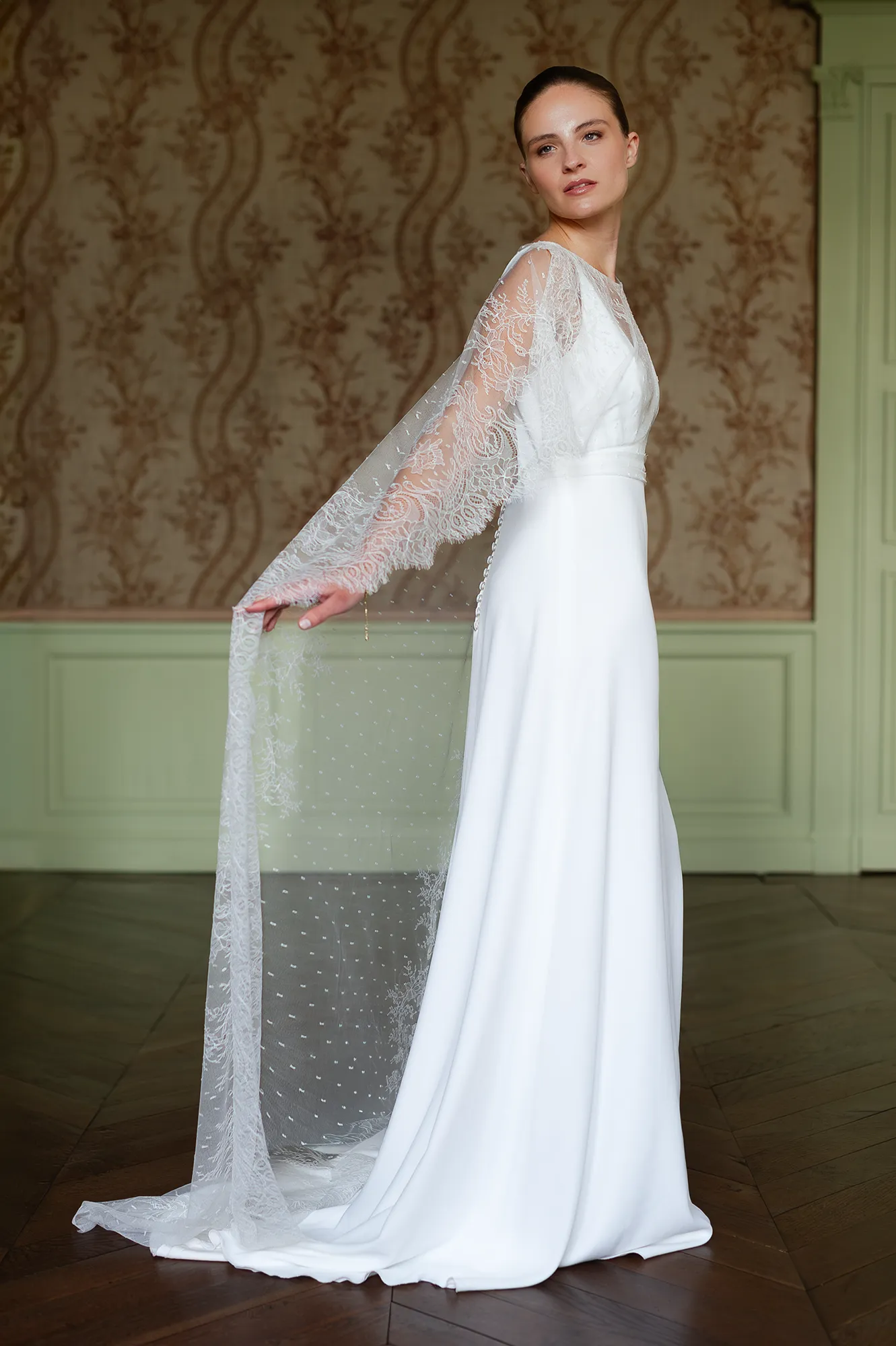 Modèle Iria en vue de profil, cape longue en tulle brodé tenue à la main et silhouette fluide. Création Louise Dentelle à Toulouse.