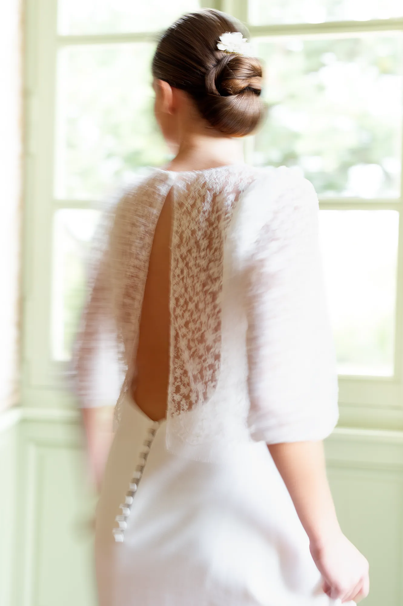 Dos du modèle Theresa avec paletot en dentelle, ouverture centrale et boutons recouverts, capté dans un mouvement flou. Création Louise Dentelle à Toulouse.